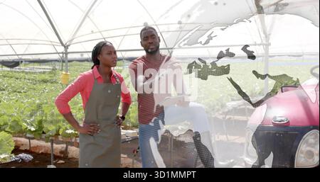 Inspecting lettuce inside tunnel greenhouse, workers wearing red shirts using tablet near tractor Stock Photo