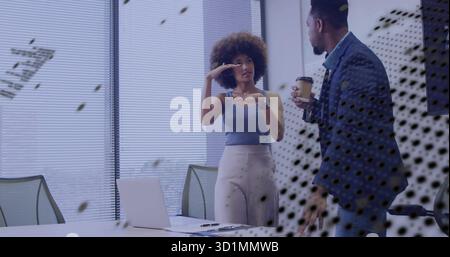 Gesturing Hispanic woman and man in suit holding coffee cup talking in meeting room, with laptop Stock Photo