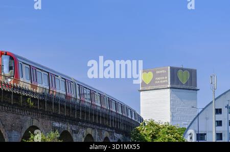 London, England - June 15, 2023: A train passes in North Kensington with the Forever in our hearts support banner visible on the Grenfell tower in the Stock Photo