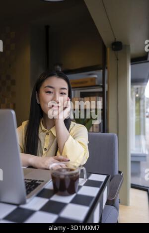 Calm Asian young female sitting in front of the portable computer in a coffee shop Stock Photo