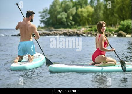 Couple of tourists young man and woman having fun paddleboarding at sea, enjoying summer vacation, active lifestyle Stock Photo