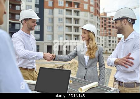 Smiling cheerful construction worker greeting a female supervisor in the presence of his male colleagues Stock Photo