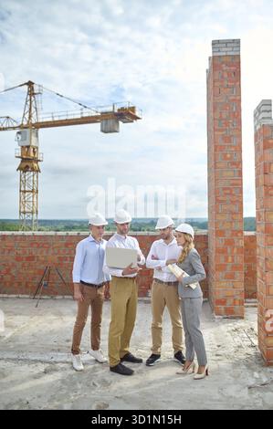 Serious focused worker showing something on his laptop to two builders and a female supervisor Stock Photo