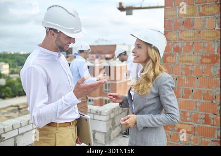 Smiling pleased elegant supervisor having a conversation with one of builders on the construction site Stock Photo