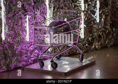 A futuristic art installation featuring a shopping cart with neon purple lights and a large disco ball, set against a metallic, reflective backdrop. T Stock Photo