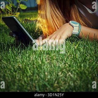 Digital education. Young lady learning using digital media in park. Student lying on grass with tablet PC Stock Photo