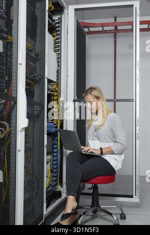 Portrait of technician working on laptop in server room Stock Photo