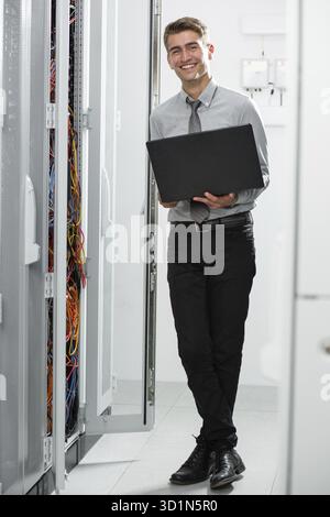 Portrait of modern young man holding laptop standing in server room working with supercomputer Stock Photo