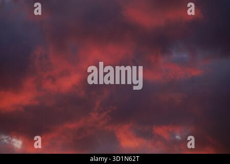 Blood red, amber orange, shades of purple, and dark blue hues mix and mesh in transitioning clouds of a fiery predawn sky showing spots of light blue. Stock Photo
