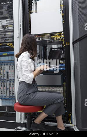Technician apecialist woman using laptop while analyzing server in server room Stock Photo