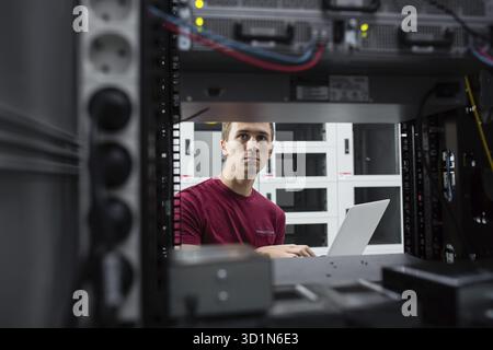 Young man connecting wires in server cabinet while working with supercomputer in data center Stock Photo
