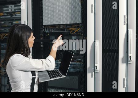 Technician apecialist woman using laptop while analyzing server in server room Stock Photo