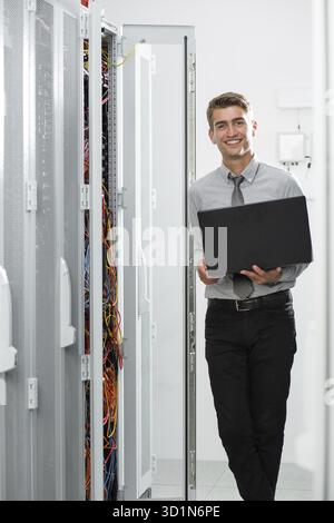 Male Server Engineer Works on a Laptop in Large Data Center Stock Photo