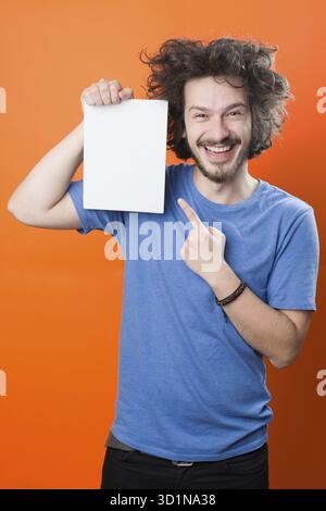 Bearded man with mustache and funny hair holding blank white board on orange background Stock Photo
