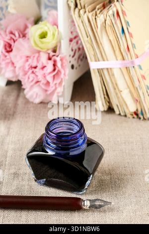 Bottle of ink, vintage pen and stack od letters in the background. Stock Photo