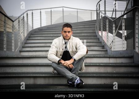 Young man in casual clothes sitting cross legged on stairway. Stock Photo