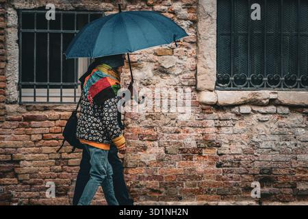 A couple Walking with Blue Umbrella beside Old Brick Wall in Venice, Italy Stock Photo