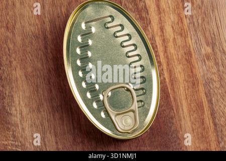 Closed oval tin can of tuna fish with round pull tab on wooden table. Metallic texture of easy-open lid. Top view Stock Photo