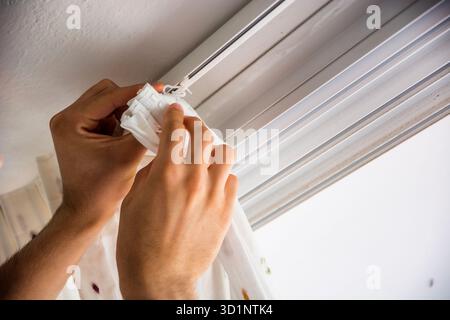 Hands of man installing curtains over window Stock Photo