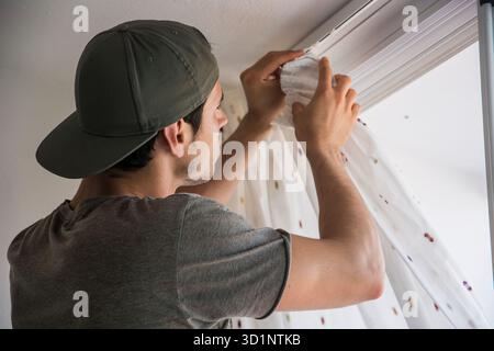 Young man installing curtains over window Stock Photo