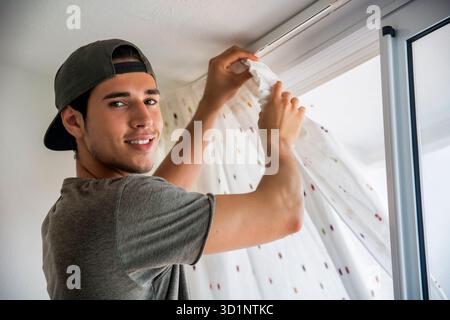 Young man installing curtains over window Stock Photo