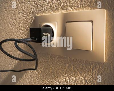 Wall electrical socket and light switch with 25W charger plugged in Stock Photo