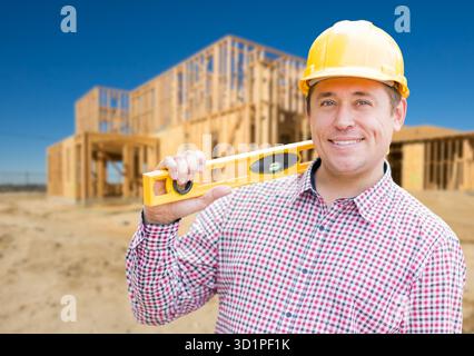 Smiling Male Contractor in Hardhat Holding Blueprints  and Level at Home Construction Site. Stock Photo
