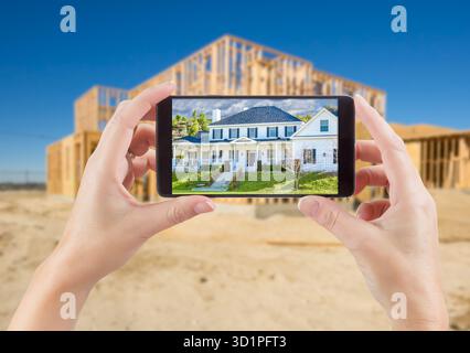 Female Hands Holding Smart Phone Displaying Photo of House with Unfinished Home Construction Behind. Stock Photo