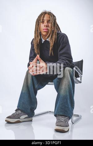 Young man with dreadlocks sitting pensive in studio Stock Photo