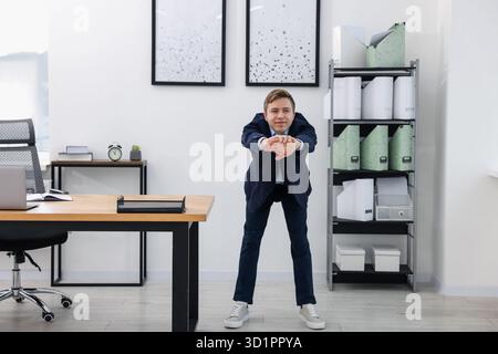 Young businessman doing stretching exercise in office Stock Photo