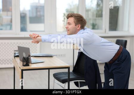 Young businessman doing stretching exercise in office Stock Photo