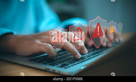 Hands typing on laptop with cybersecurity alert icons. Concept of online data protection, system security warning, and internet risk prevention. Stock Photo