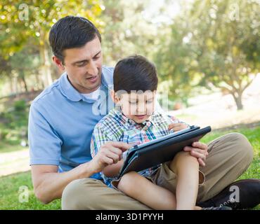 Happy Father and Son Playing on a Computer Tablet Outside. Stock Photo
