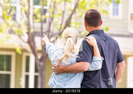 Happy Caucasian Couple Facing and Pointing to Front of House Stock Photo