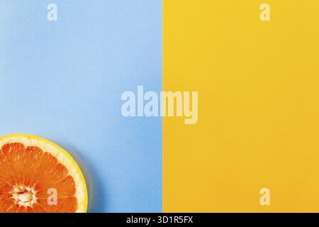 Top view of single grapefruit slice close-up on blue and yellow background. . Minimalist picture style with copy space for text Stock Photo