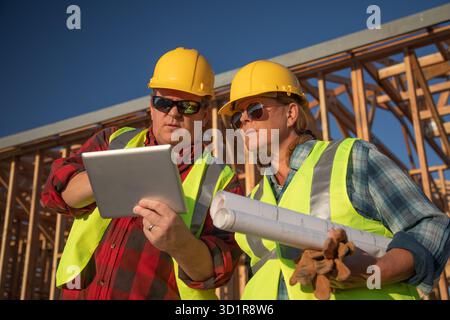 Male and Female Construction Workers Using Computer Pad at Construction Site Stock Photo