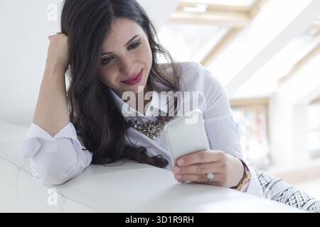 Young attractive woman sitting on sofa at home, talking on mobile phone Stock Photo