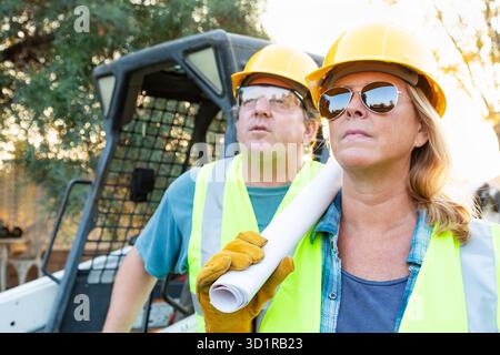 Male and Female Workers With Technical Blueprints at Construction Site Stock Photo
