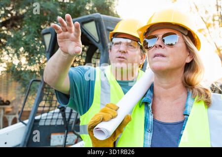 Male and Female Workers With Technical Blueprints Talking at Construction Site Stock Photo