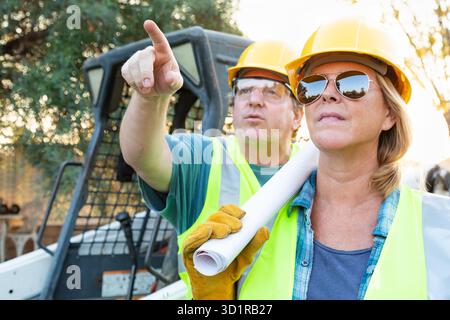 Male and Female Workers With Technical Blueprints Talking at Construction Site Stock Photo