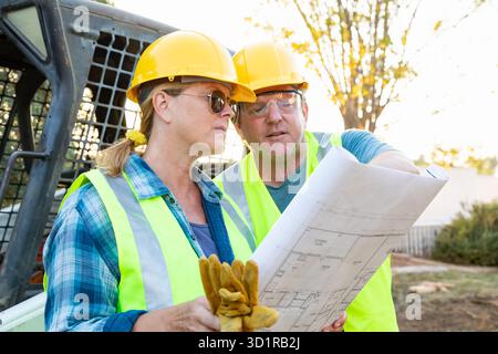 Male and Female Workers With Technical Blueprints Talking at Construction Site Stock Photo
