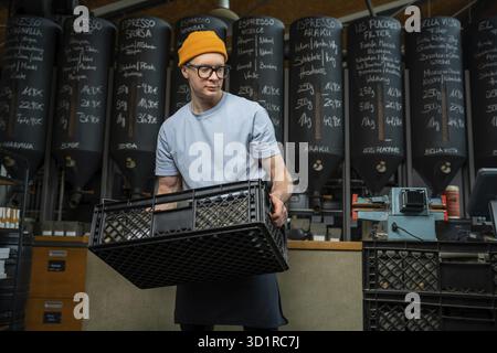 Caucasian man wearing hat apron and glasses coffee shop worker gets new batch of coffee packages in boxes on roasting factory Stock Photo
