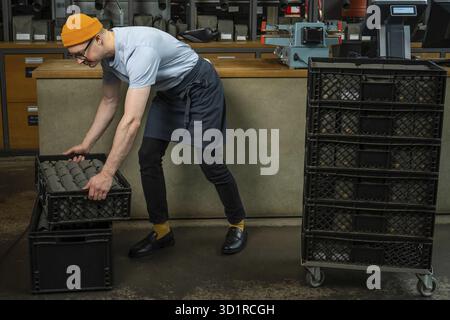 Male worker or business owner uploads packages of coffee on factory or warehouse, barista in coffee shop Stock Photo