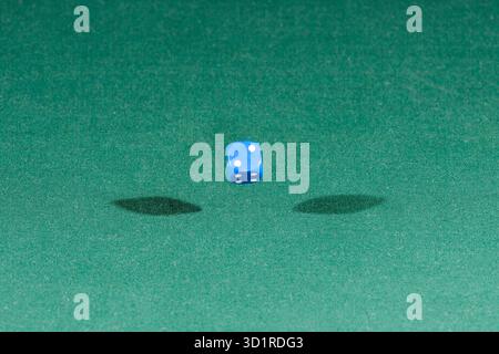 One blue dice falling on a green table Stock Photo