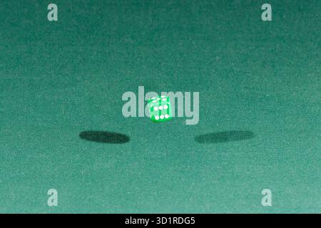 One green dice falling on a green table Stock Photo