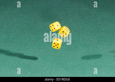 Three yellow dices falling on a green table Stock Photo