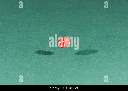 One red dice falling on a green table Stock Photo
