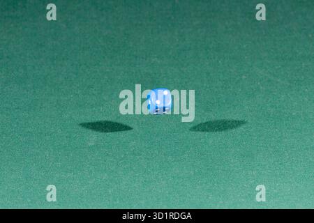 One blue dice falling on a green table Stock Photo