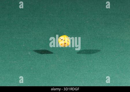 One yellow dice falling on a green table Stock Photo