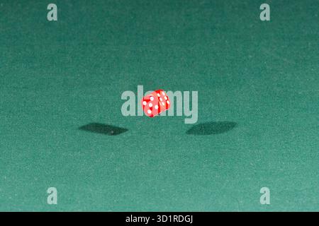 One red dice falling on a green table Stock Photo